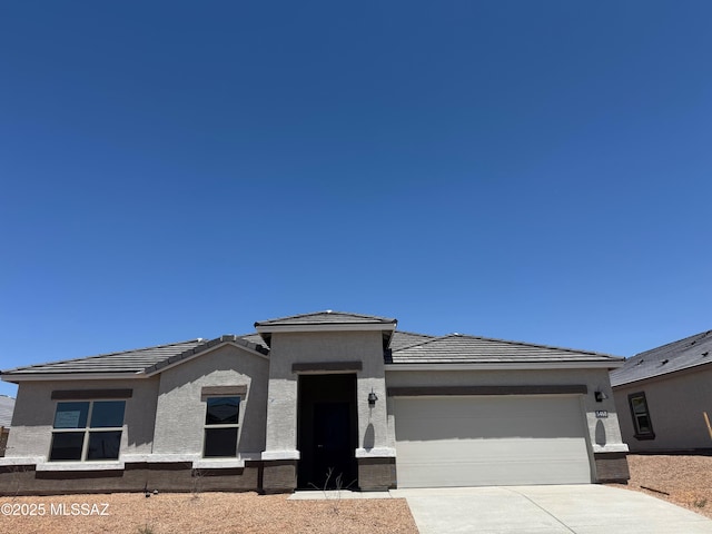 prairie-style house featuring an attached garage, stucco siding, a tile roof, and concrete driveway