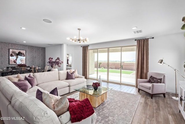 living area featuring a chandelier, an accent wall, wallpapered walls, wood finished floors, and visible vents