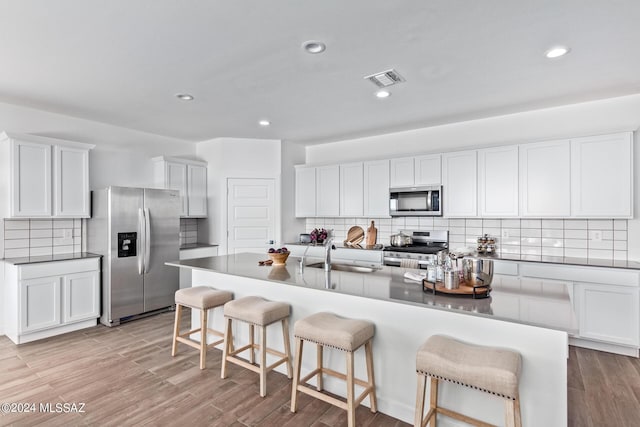 kitchen with decorative backsplash, a breakfast bar, white cabinetry, a sink, and appliances with stainless steel finishes