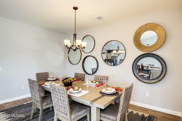 dining space with visible vents, baseboards, wood finished floors, and a notable chandelier