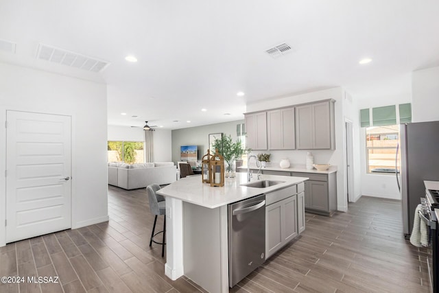 kitchen featuring sink, a breakfast bar area, appliances with stainless steel finishes, gray cabinetry, and a center island with sink