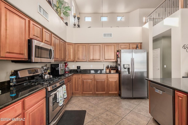 kitchen with stainless steel appliances, a towering ceiling, light tile patterned floors, and dark stone counters