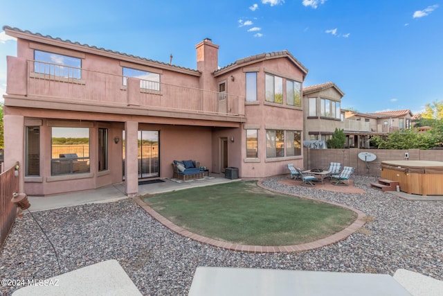 back of property featuring a balcony, an outdoor fire pit, a hot tub, and a patio