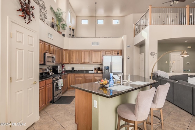 kitchen featuring light tile patterned floors, ceiling fan, a kitchen island with sink, stainless steel appliances, and a kitchen bar