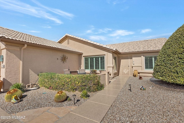 view of exterior entry featuring a patio area, a tile roof, and stucco siding