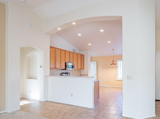 kitchen with arched walkways, vaulted ceiling, light countertops, hanging light fixtures, and stainless steel microwave