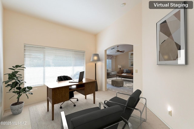 office area featuring arched walkways, lofted ceiling, a ceiling fan, and light colored carpet