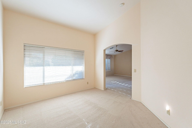 spare room featuring arched walkways, light colored carpet, ceiling fan, and lofted ceiling