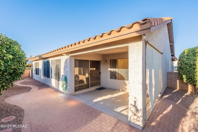 back of house with stucco siding, a tiled roof, fence, and a patio