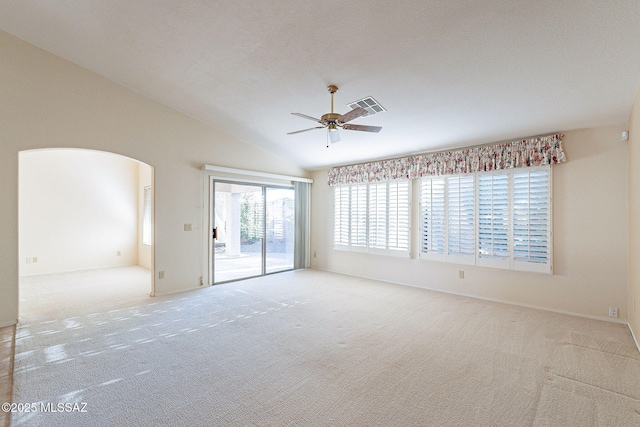 empty room with arched walkways, lofted ceiling, light carpet, visible vents, and a ceiling fan