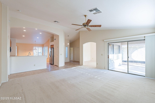 unfurnished living room with light carpet, vaulted ceiling, arched walkways, and visible vents