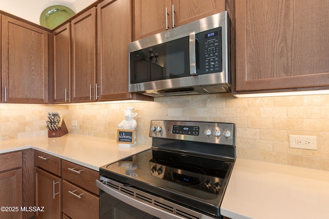 kitchen with stainless steel appliances, brown cabinetry, backsplash, and light countertops