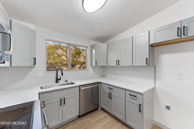 kitchen featuring tasteful backsplash, lofted ceiling, gray cabinets, appliances with stainless steel finishes, and a sink