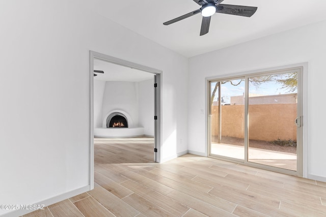 spare room featuring wood tiled floor, a fireplace, baseboards, and a ceiling fan