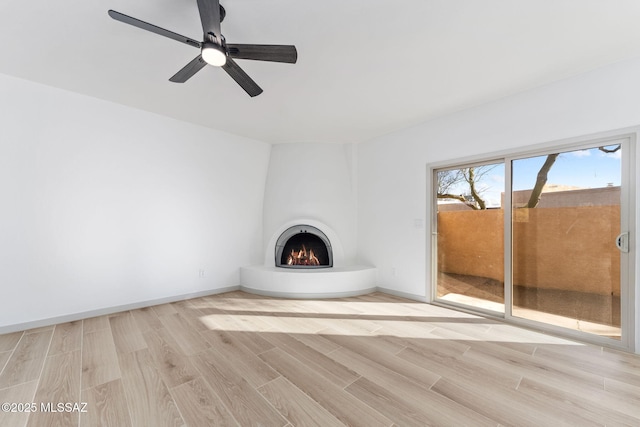 unfurnished living room with light wood finished floors, ceiling fan, baseboards, and a large fireplace