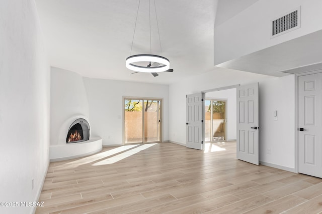 unfurnished living room with light wood-type flooring, visible vents, a fireplace, and baseboards