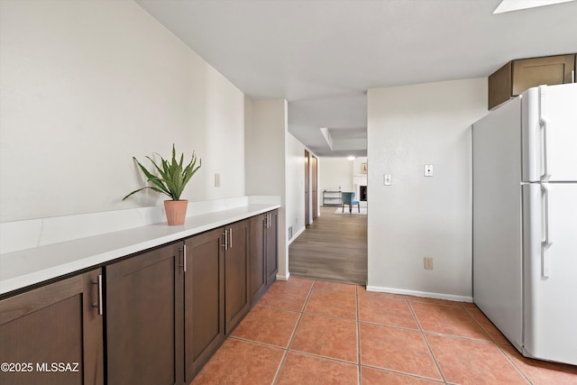 kitchen featuring white refrigerator, dark brown cabinets, and light tile patterned floors