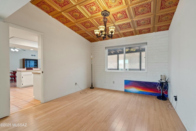 empty room with an ornate ceiling, ceiling fan with notable chandelier, and light wood finished floors