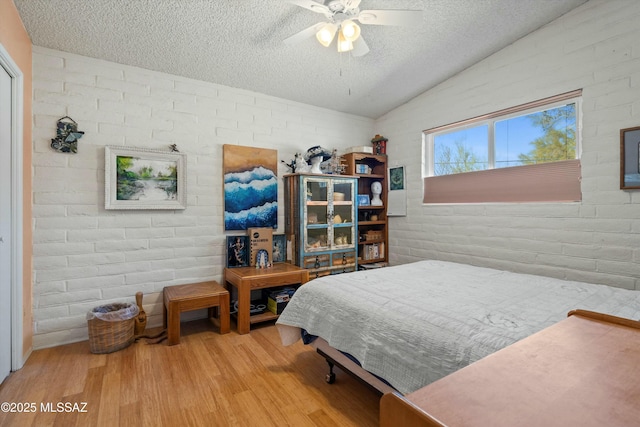 bedroom with brick wall, a textured ceiling, lofted ceiling, and wood finished floors