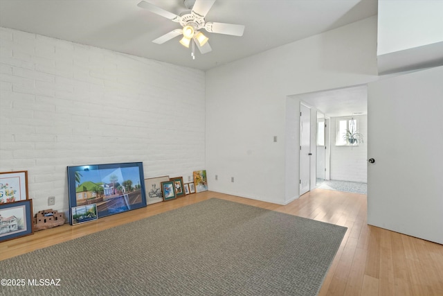 living area with wood finished floors, brick wall, and ceiling fan