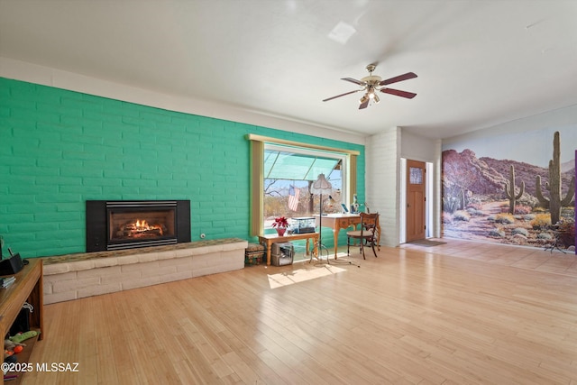 living area featuring a fireplace, a ceiling fan, and wood finished floors