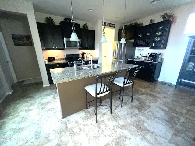 kitchen with pendant lighting, stainless steel appliances, a kitchen breakfast bar, light stone countertops, and a center island with sink