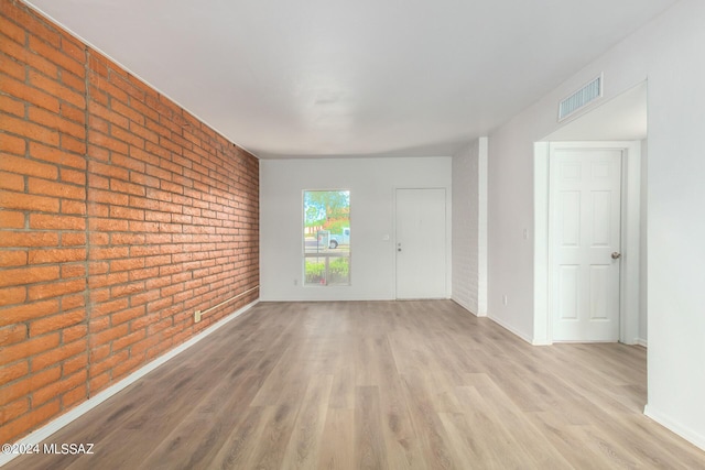 spare room featuring brick wall and light wood-type flooring