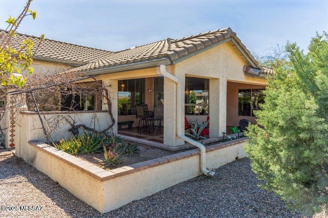 rear view of house featuring stucco siding and a tiled roof