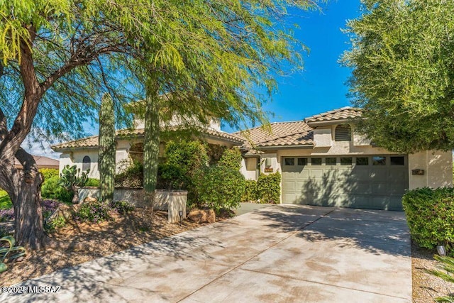 mediterranean / spanish house with an attached garage, a tile roof, concrete driveway, and stucco siding