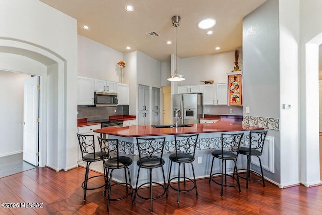 kitchen featuring white cabinets, dark countertops, a peninsula, stainless steel appliances, and a sink