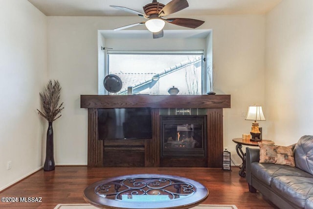 living room featuring a glass covered fireplace, wood finished floors, a ceiling fan, and baseboards