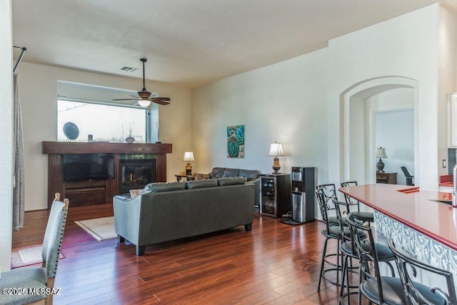 living area with arched walkways, dark wood finished floors, visible vents, a glass covered fireplace, and ceiling fan