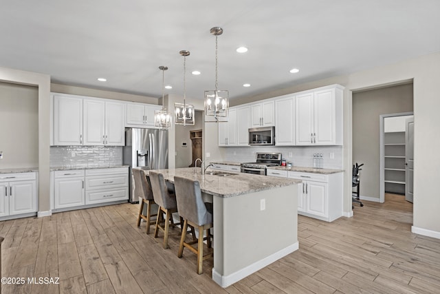 kitchen featuring appliances with stainless steel finishes, white cabinets, a sink, and light wood-style flooring