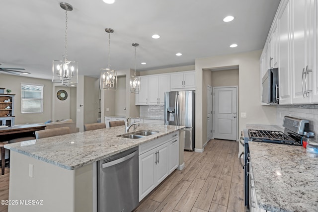 kitchen with light wood finished floors, open floor plan, stainless steel appliances, white cabinetry, and a sink