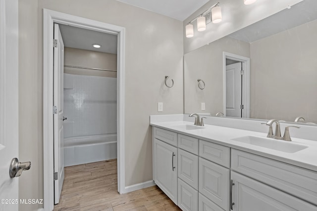 bathroom featuring double vanity, tub / shower combination, a sink, and wood finished floors