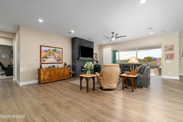 living room with a large fireplace, light wood finished floors, visible vents, and baseboards