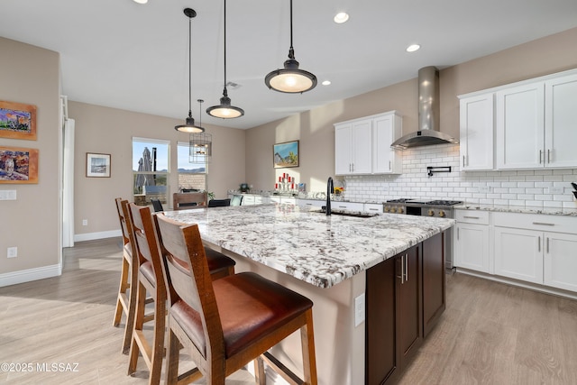 kitchen featuring wall chimney exhaust hood, a kitchen island with sink, white cabinets, and a sink