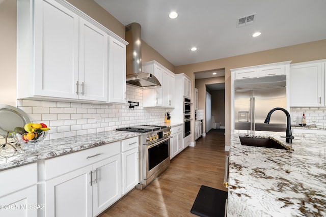 kitchen featuring visible vents, white cabinetry, a sink, wall chimney range hood, and high quality appliances