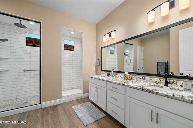 bathroom with a walk in shower, double vanity, wood finished floors, and a sink