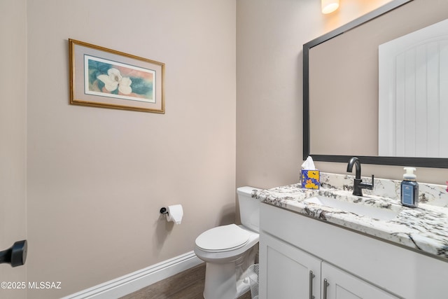 half bath featuring toilet, wood finished floors, vanity, and baseboards