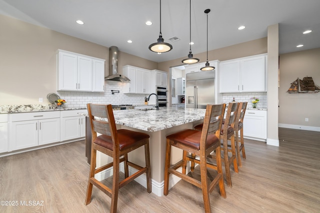 kitchen with pendant lighting, wall chimney range hood, appliances with stainless steel finishes, and white cabinets