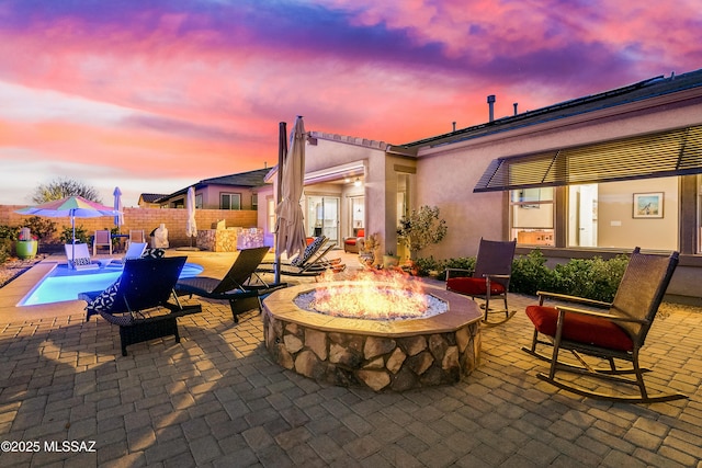 patio terrace at dusk featuring an outdoor fire pit and fence