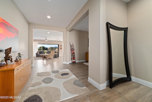 hallway featuring light wood finished floors, baseboards, and recessed lighting