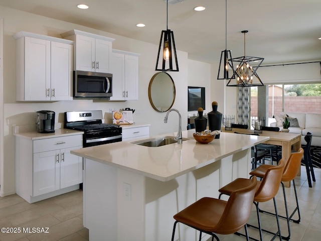 kitchen featuring appliances with stainless steel finishes, a center island with sink, a sink, and white cabinetry