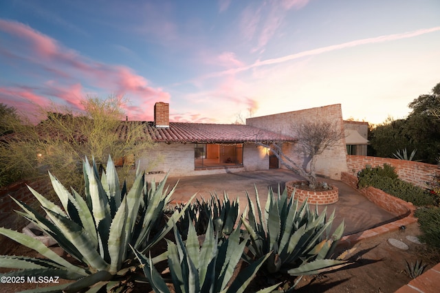 back of house at dusk with a patio, brick siding, fence, a tiled roof, and a chimney