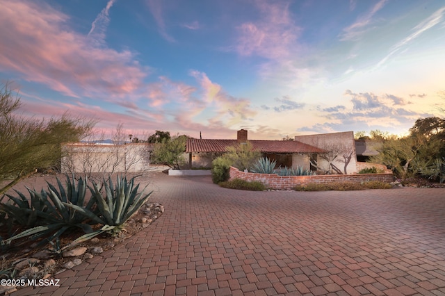 view of front of home featuring decorative driveway, a chimney, and stucco siding