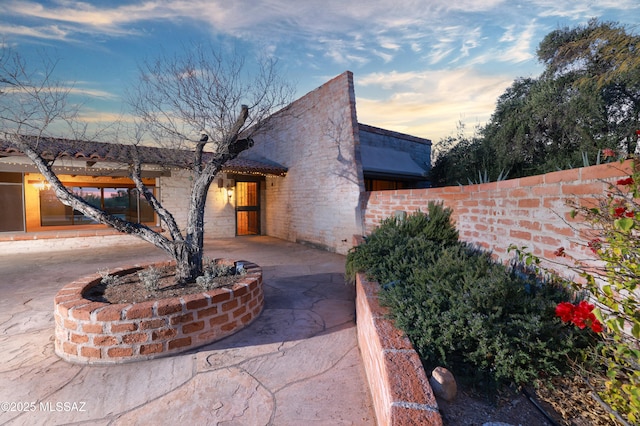 view of front of home with stone siding, fence, and a patio