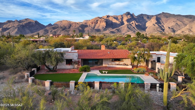 rear view of property featuring a chimney, a mountain view, an outdoor pool, and a tiled roof