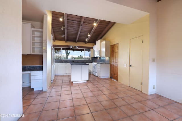 kitchen with white appliances, built in study area, dark countertops, beamed ceiling, and white cabinetry