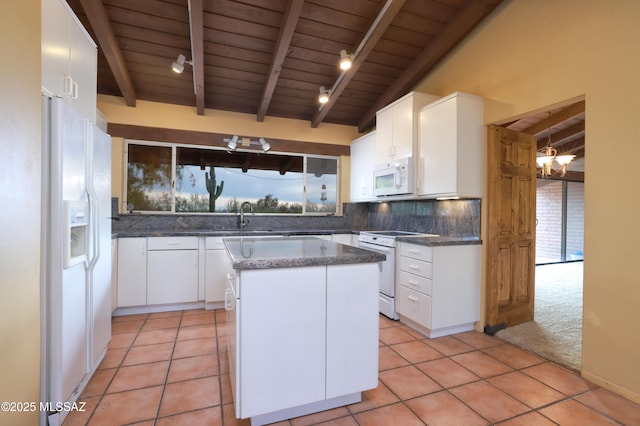 kitchen featuring white appliances, tasteful backsplash, lofted ceiling with beams, a center island, and white cabinetry